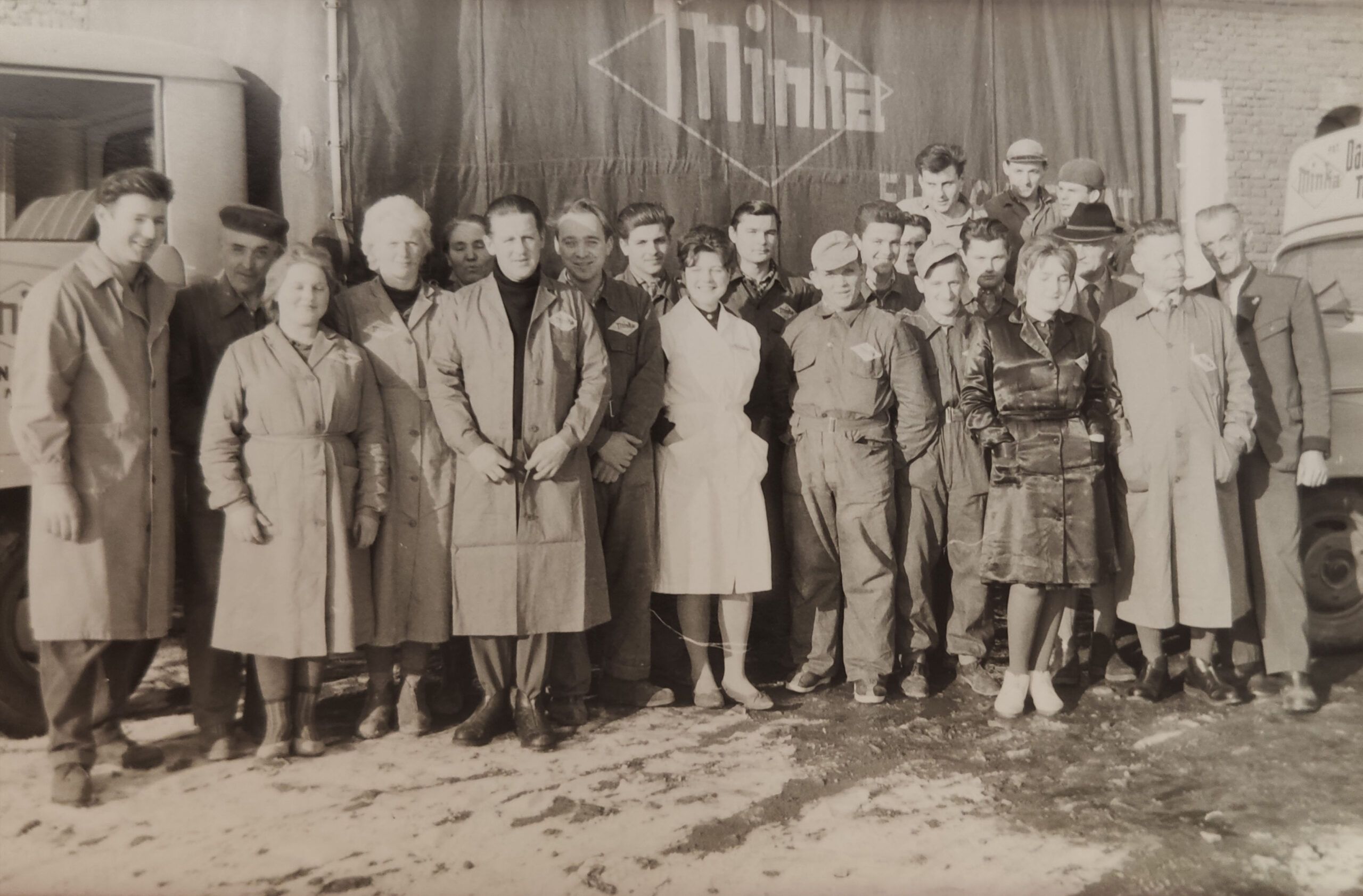 About 20 men and women in work clothes are standing in front of a truck with the Minka logo.