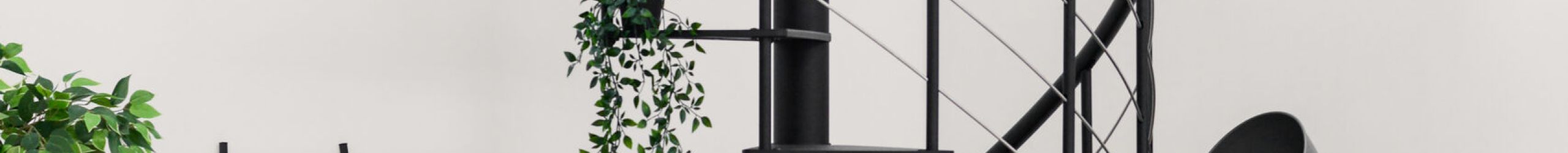 Modern “Milano” spiral staircase made of black metal. The staircase features open metal steps, a railing with vertical rods, horizontal base bars (underguards), and a black PVC handrail.