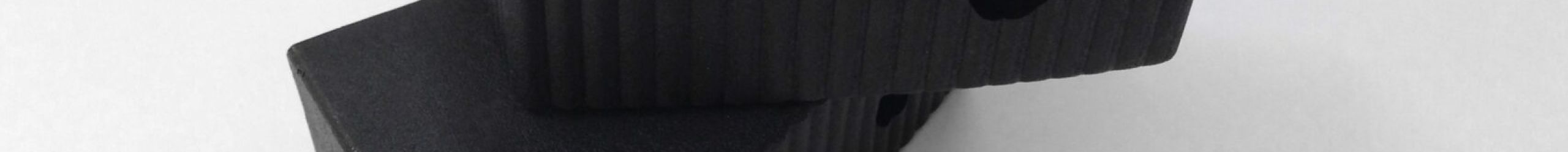 Two black stair shoes for wooden stairs with a ribbed surface, including two mounting screws, placed on a light background.