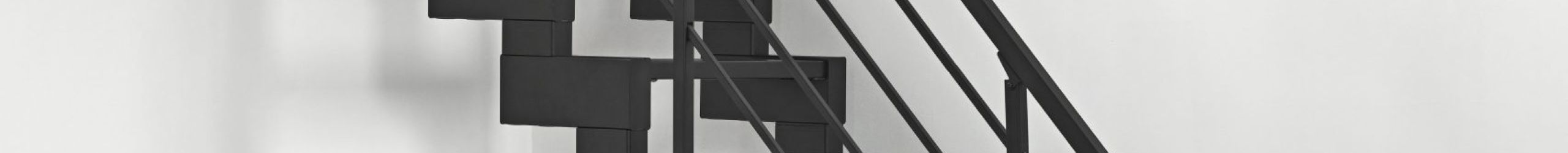 Modulario Mini straight space-saving staircase in black with metal treads. The staircase is mounted on a white wall and stands on a light-coloured wooden floor. The modern metal banister provides a secure hold.