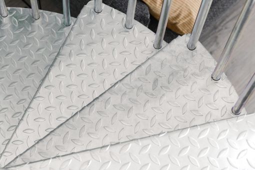 Close-up view of galvanized metal steps with anti-slip diamond plate pattern and vertical balusters from the Rondo Zink Smart spiral staircase.