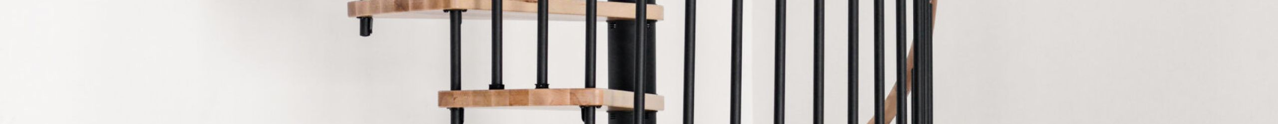 Spiral staircase Spiral Wood with steps and handrail made of solid beech wood and vertical balusters and spindle tubes in black powder-coated steel, installed in a white room.