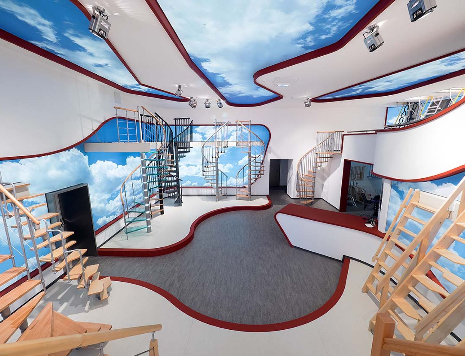 Wide-angle view of the modern Minka showroom featuring various staircase models. The sky-themed walls and ceiling create an open, inspiring atmosphere.