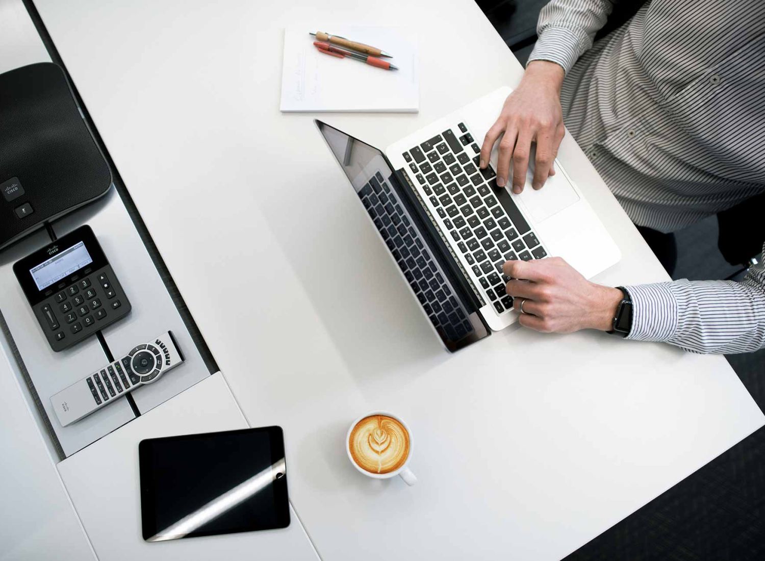 Man sitting at a white desk and typing something on a laptop