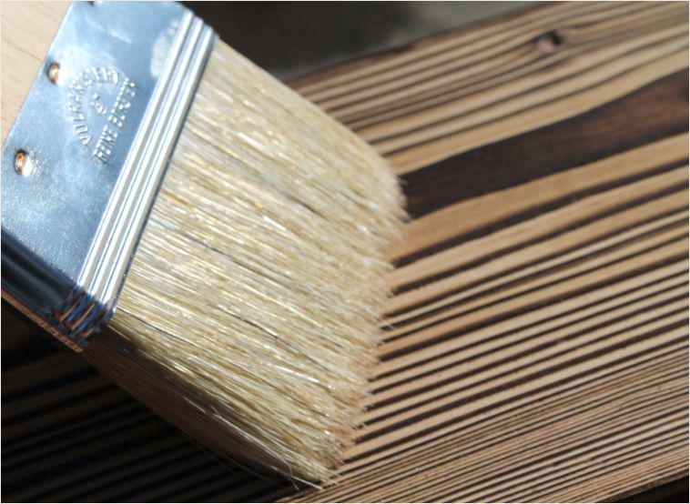 Close-up of a brush applying protective coating on a wooden surface.