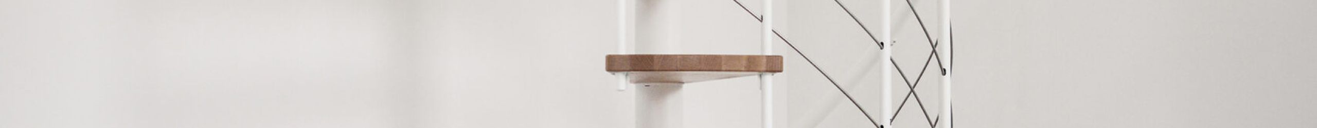 Spiral staircase Venezia Smart with beech wood steps, white metal parts, white PVC handrail and stainless steel bottom rails, installed in a white room.