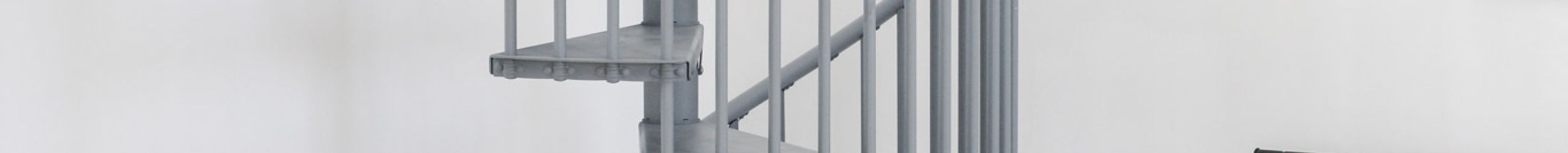 Grey metal spiral staircase Rondo Smart with round steps and vertical railing rods. The space-saving staircase winds upwards in a modern living area with sofa, plants and a clothes rack.