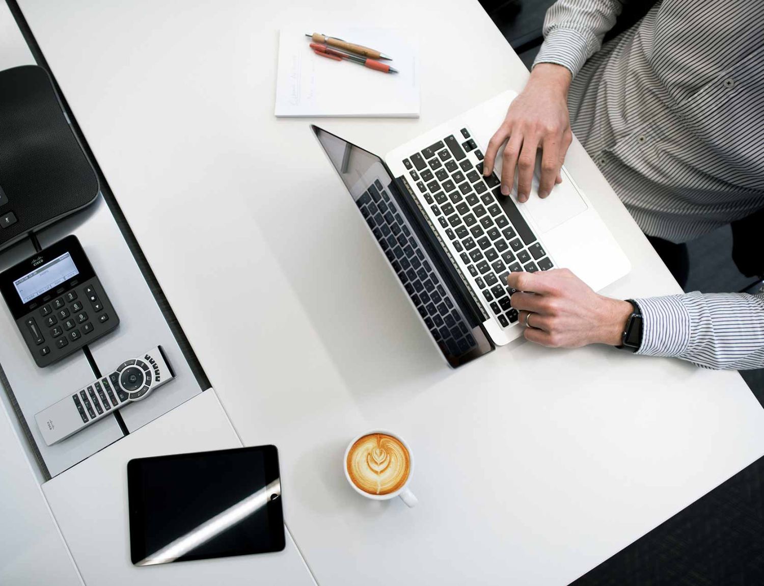 Man sitting at a white desk and typing something on a laptop