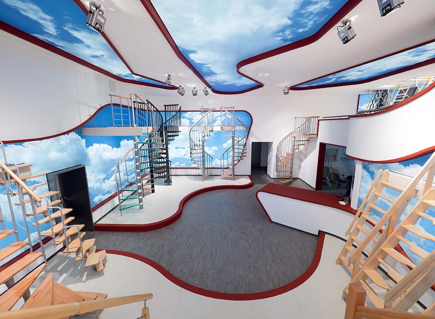 Wide-angle view of the modern Minka showroom featuring various staircase models. The sky-themed walls and ceiling create an open, inspiring atmosphere.