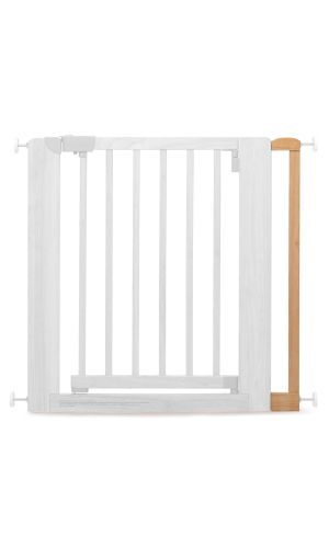 A toddler plays with colorful toys on the floor in front of the mounted "Annika" wooden child safety gate. The gate is installed between two walls, separating the play area from the kitchen behind.