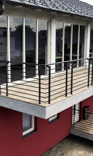 Modern Orion-Top balustrade in anthracite on a spacious balcony with wooden decking and concrete slab. The vertical posts are mounted on the balcony surface and support horizontal, evenly arranged struts. The railing emphasizes the contemporary, clear architectural style of the building.