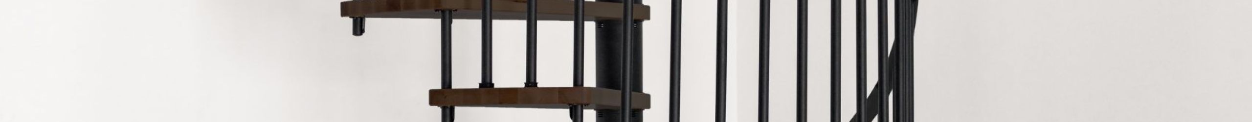 Spiral staircase Spiral Wood with dark steps in walnut look and black steel banister with aluminium handrail, installed in a room with a grey floor and white walls.