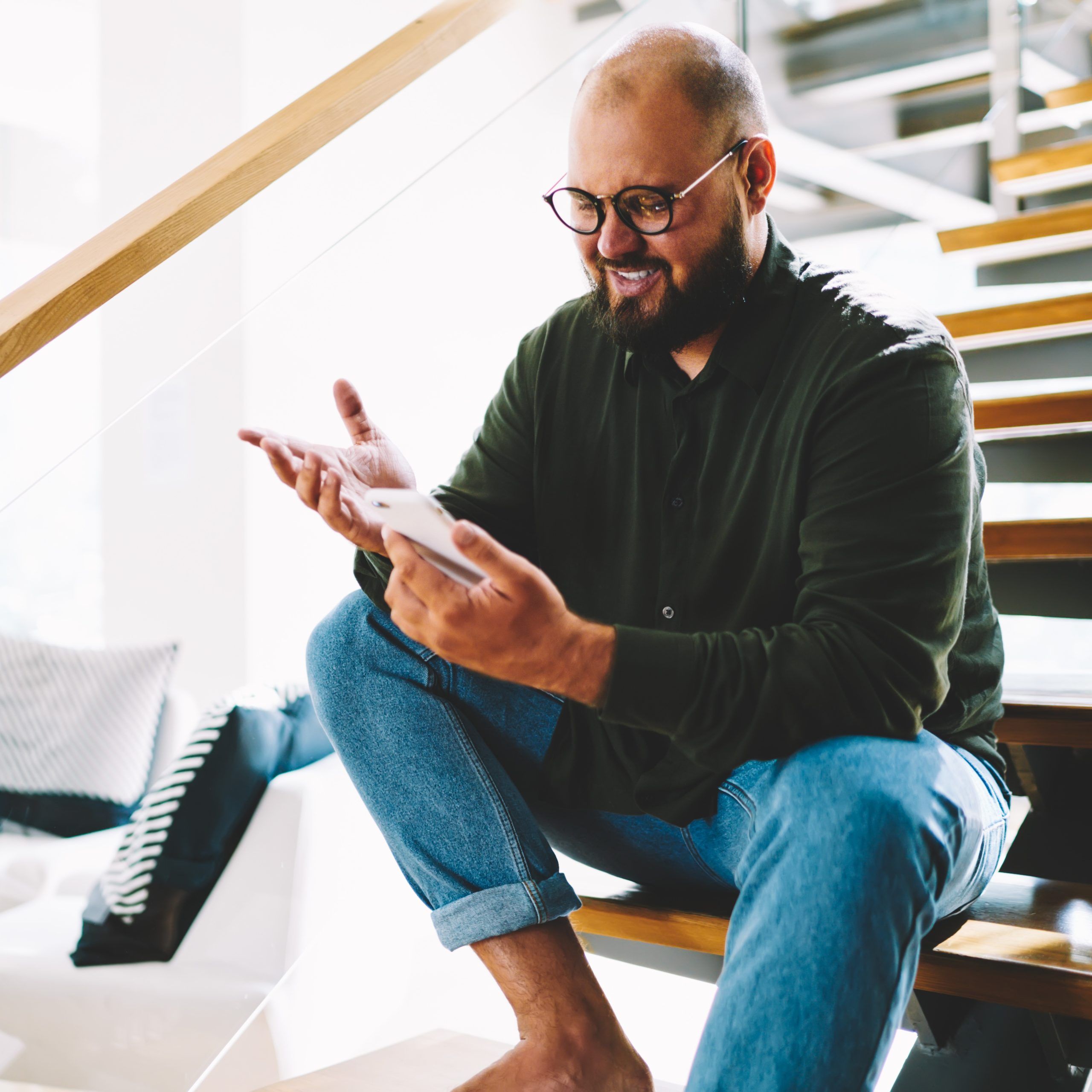 Man sits with a smartphone on a modern centre stringer staircase and smiles while looking at the display