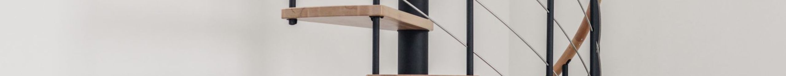 Spiral staircase Venezia with steps and handrail in beech wood, black metal parts and stainless steel bottom rails, installed in a white room.