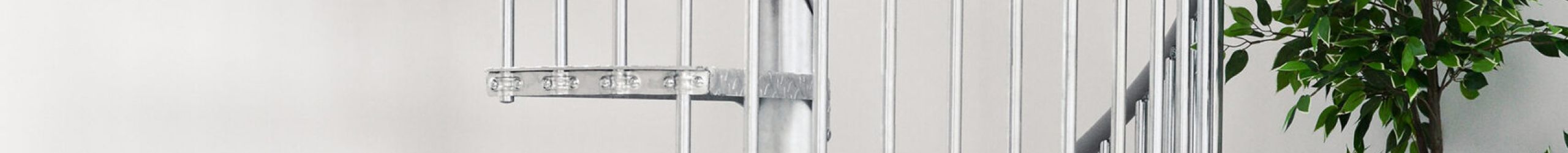 Outdoor spiral staircase Rondo Zink Smart made of galvanized metal in a modern living space. The spiral staircase leads upwards, with plants, a rug and a grey sofa with cushions in the foreground.