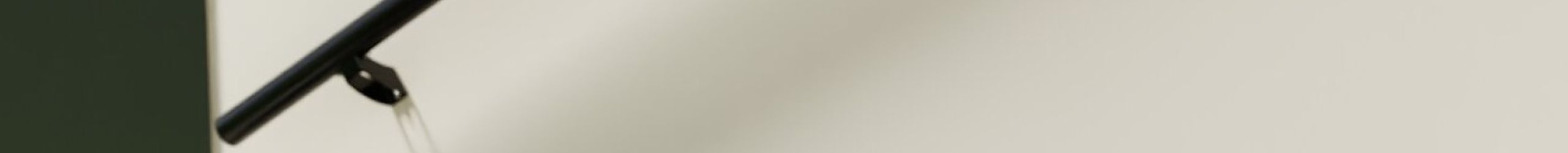 Side view of the Sirius handrail in anthracite, mounted on a light-colored wall along a modern staircase with dark steps and contrasting white stringers. The handrail is sleek, round, and supported by minimalist wall brackets.