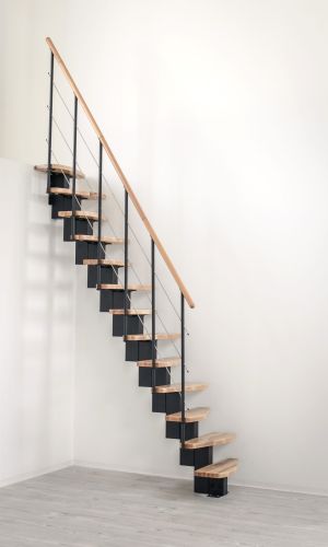 A toddler plays with colorful toys on the floor in front of the mounted "Annika" wooden child safety gate. The gate is installed between two walls, separating the play area from the kitchen behind.