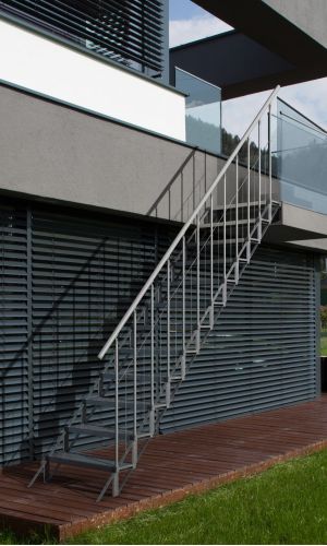A toddler plays with colorful toys on the floor in front of the mounted "Annika" wooden child safety gate. The gate is installed between two walls, separating the play area from the kitchen behind.