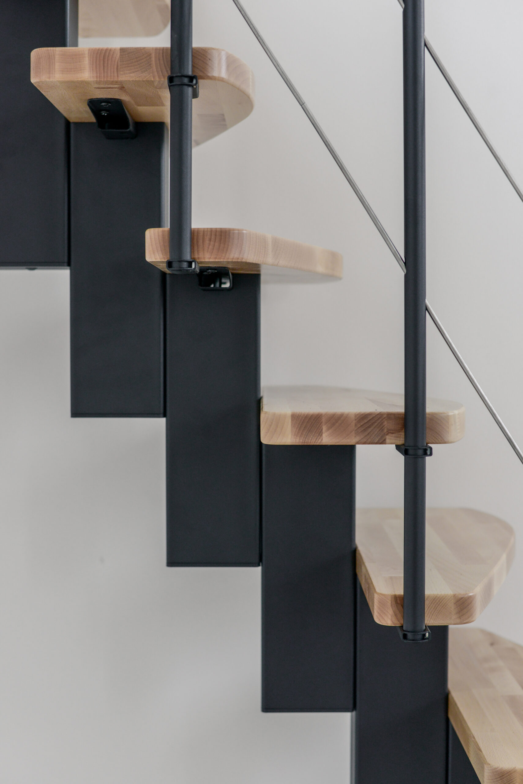 Detailed view of the Quatro central stringer staircase with light beech steps, black metal central stringer, and side railing with horizontal bars.