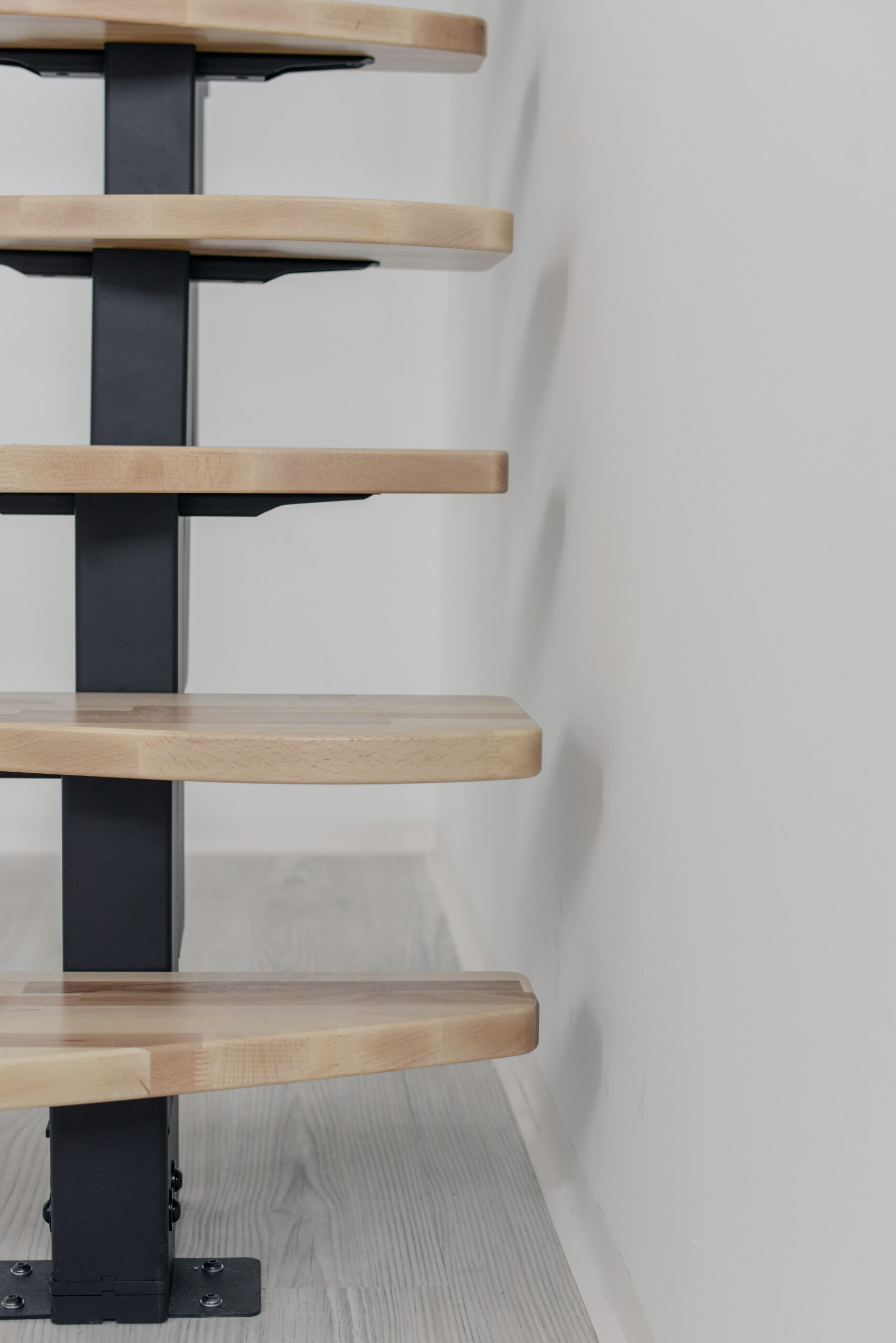 Frontal view of the lower steps of the Quatro central stringer staircase with light beech steps and a black metal central stringer.