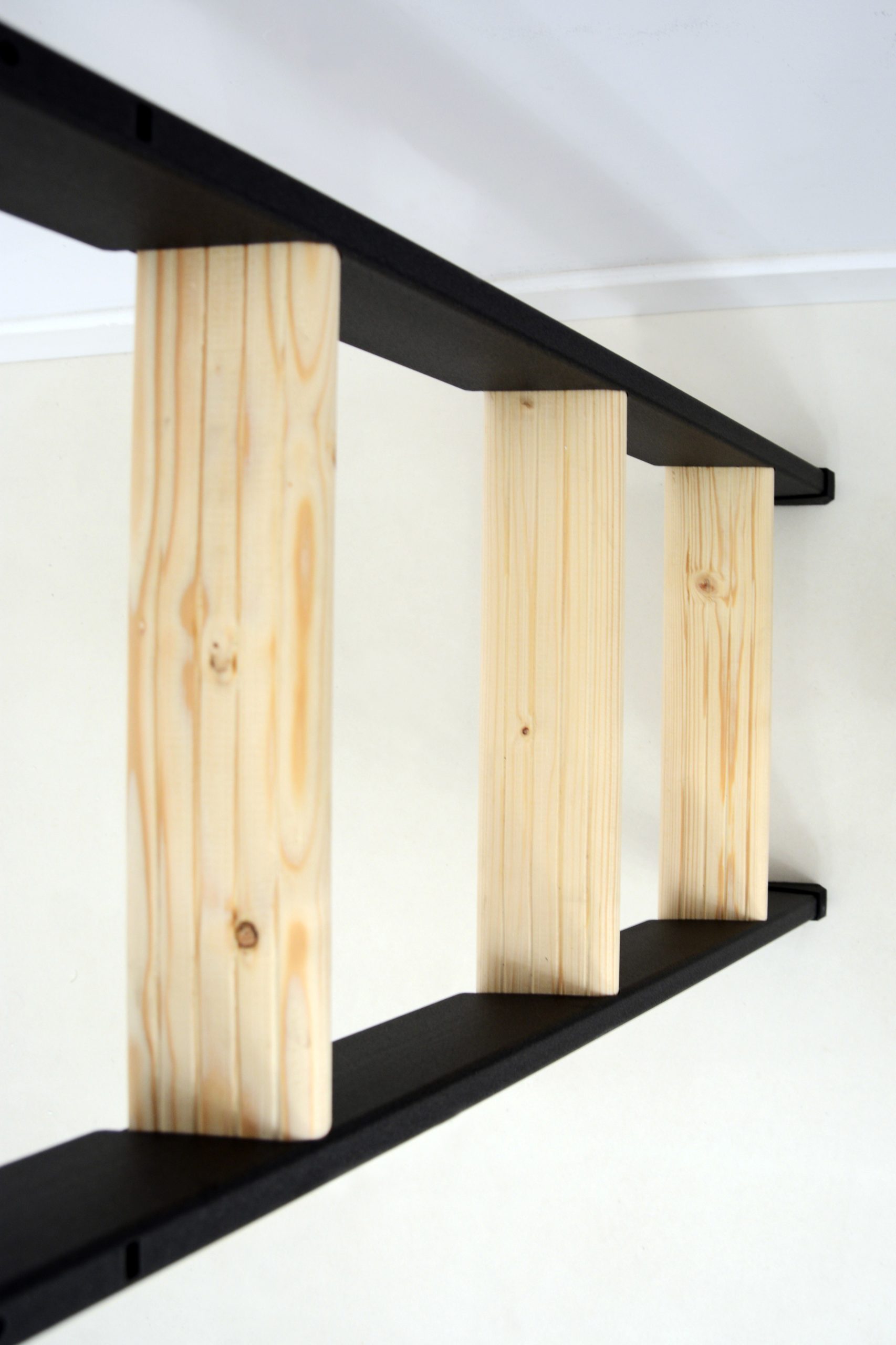 Detail view of the Strong space-saving staircase in spruce with a black metal frame. Visible are the rectangular, solid wood steps securely mounted between the side metal stringers.