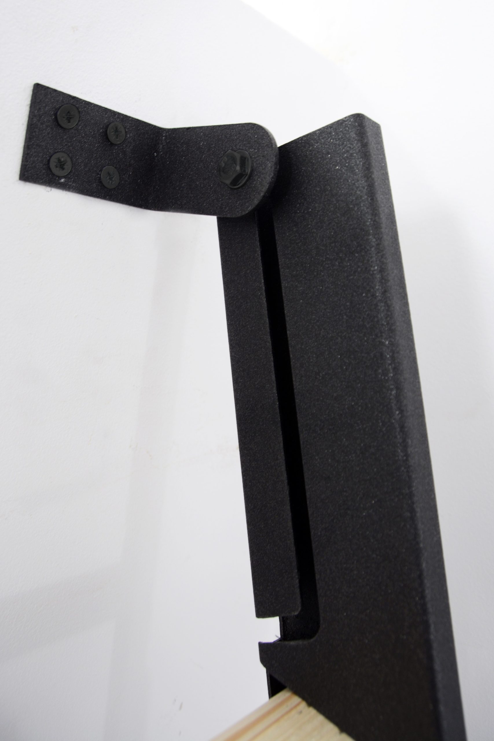 Detail view of the Strong space-saving staircase in spruce with a black metal frame. Shown is the sturdy wall bracket made of powder-coated steel for secure mounting of the staircase.