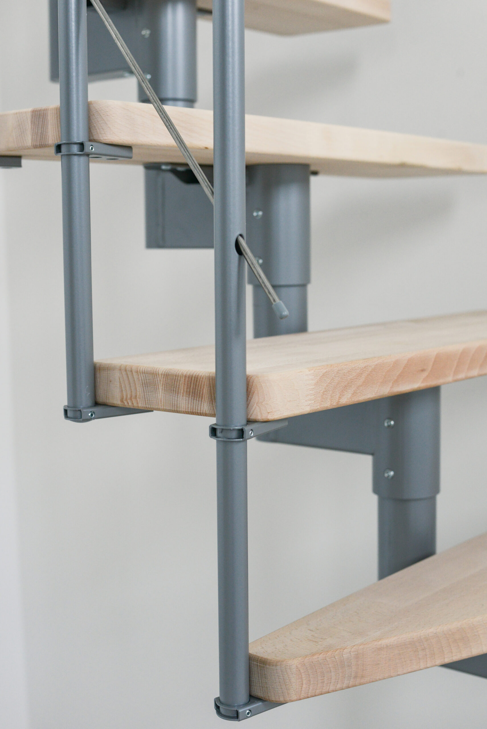 Close-up of the Style Turn staircase with walnut steps and a gray metal structure. The steps are attached to sturdy metal posts, and the horizontal stainless steel cables provide additional stability and safety.