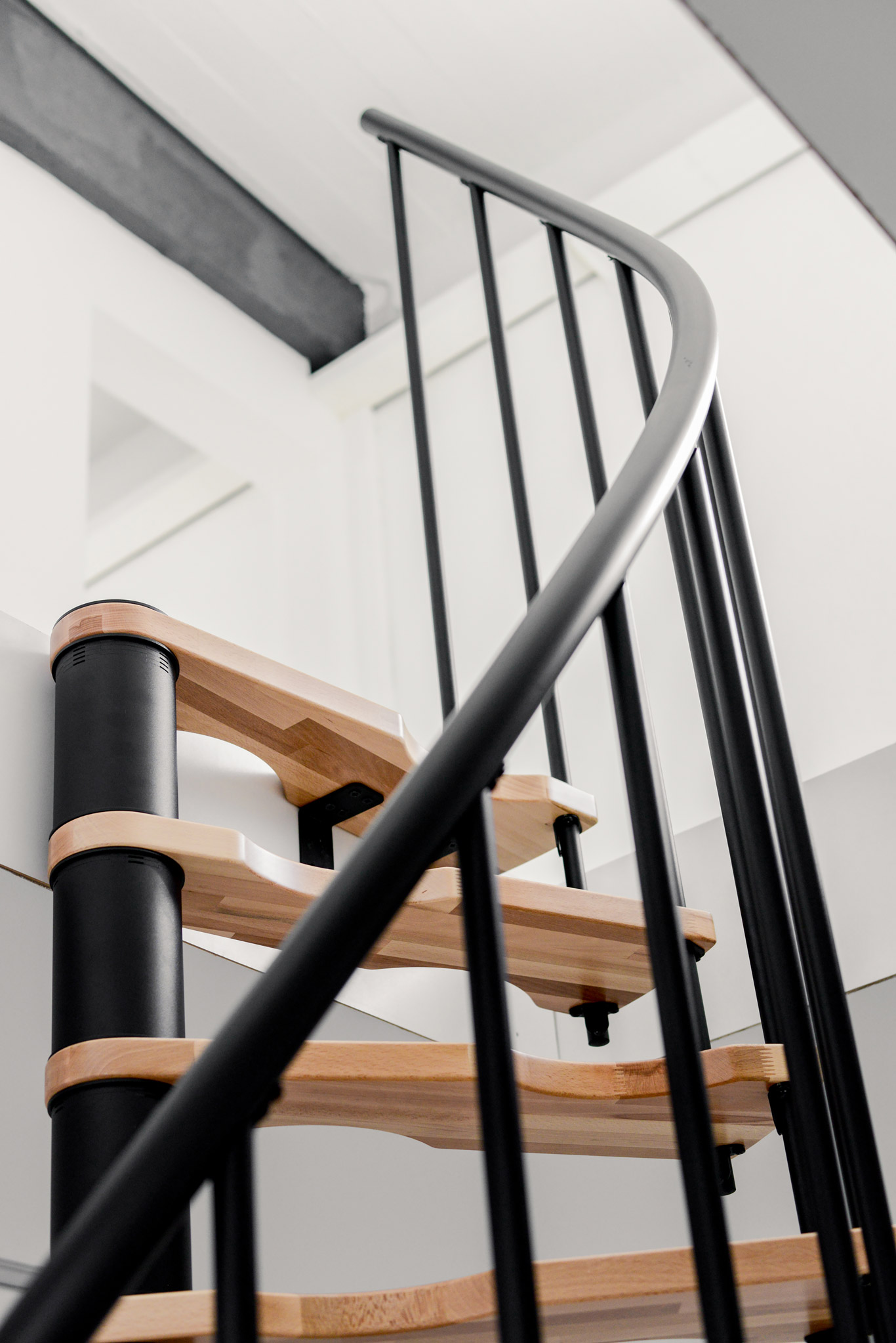 Close-up of the Suono Smart spiral staircase with curved black handrail, black railing rods, and light wooden steps – modern design in a compact form.