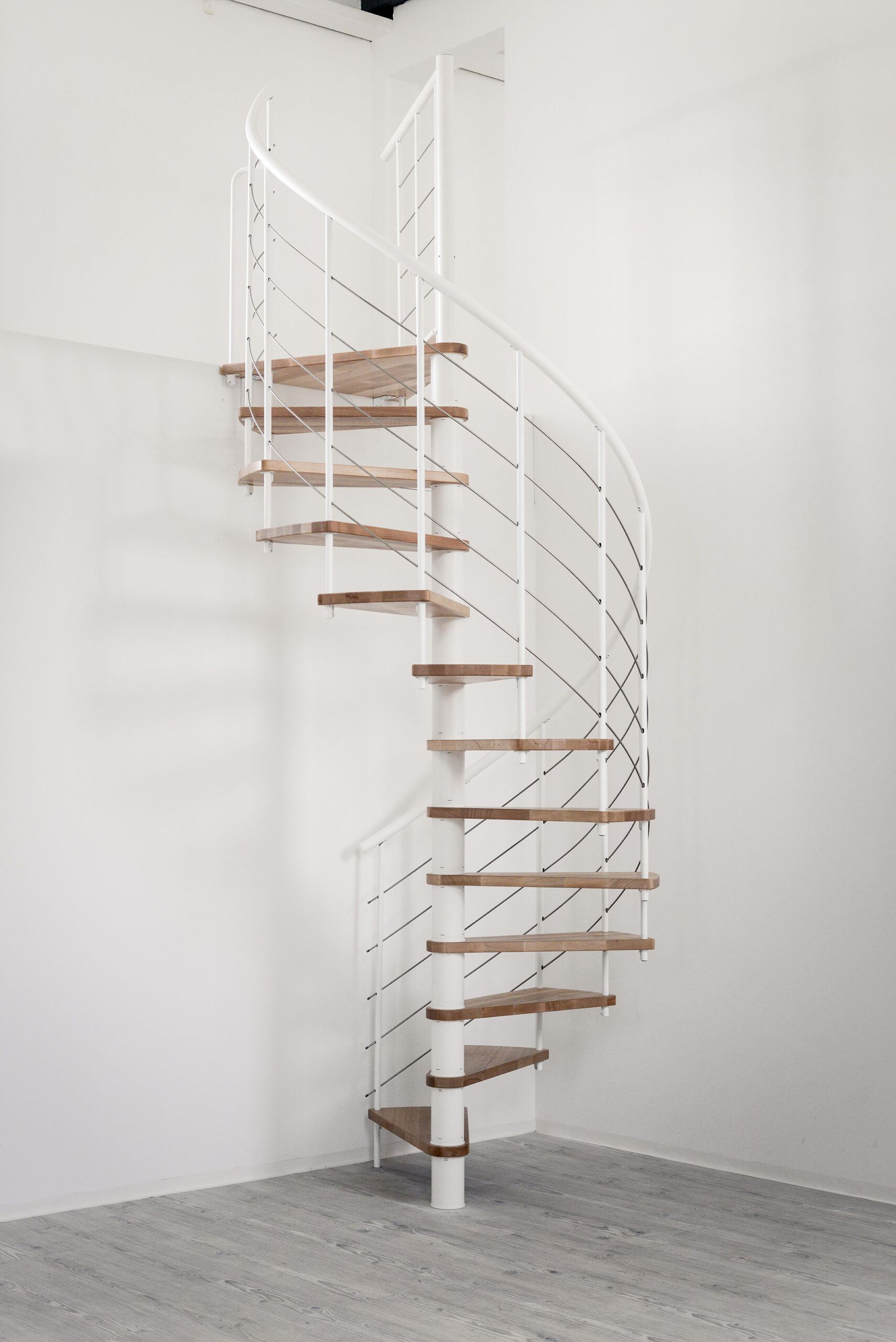 Spiral staircase Venezia Smart with beech wood steps, white metal parts, white PVC handrail and stainless steel bottom rails, installed in a white room.