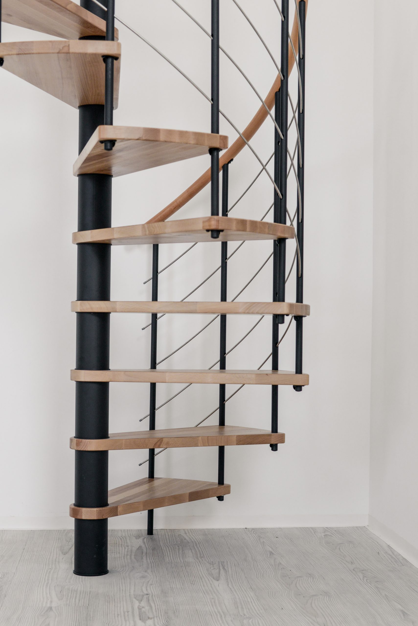 Height-adjustable spindle tubes of the spiral staircase Venezia in black powder-coated with steps made of beech wood and steel railing in a white room