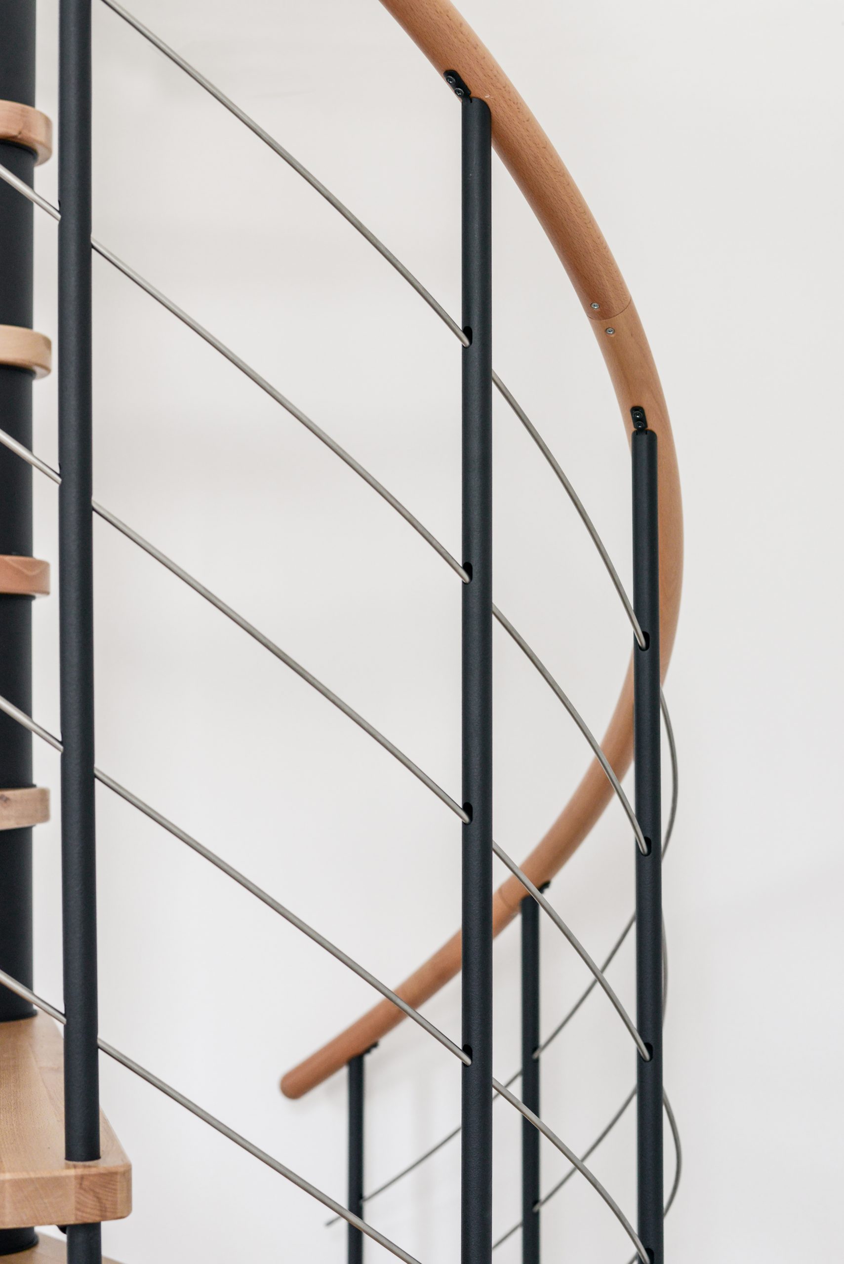 Close-up of the banister of the Venezia spiral staircase. The vertical rods made of black powder-coated steel are crossed horizontally by 5 stainless steel bottom rails. The handrail is made of beech wood.
