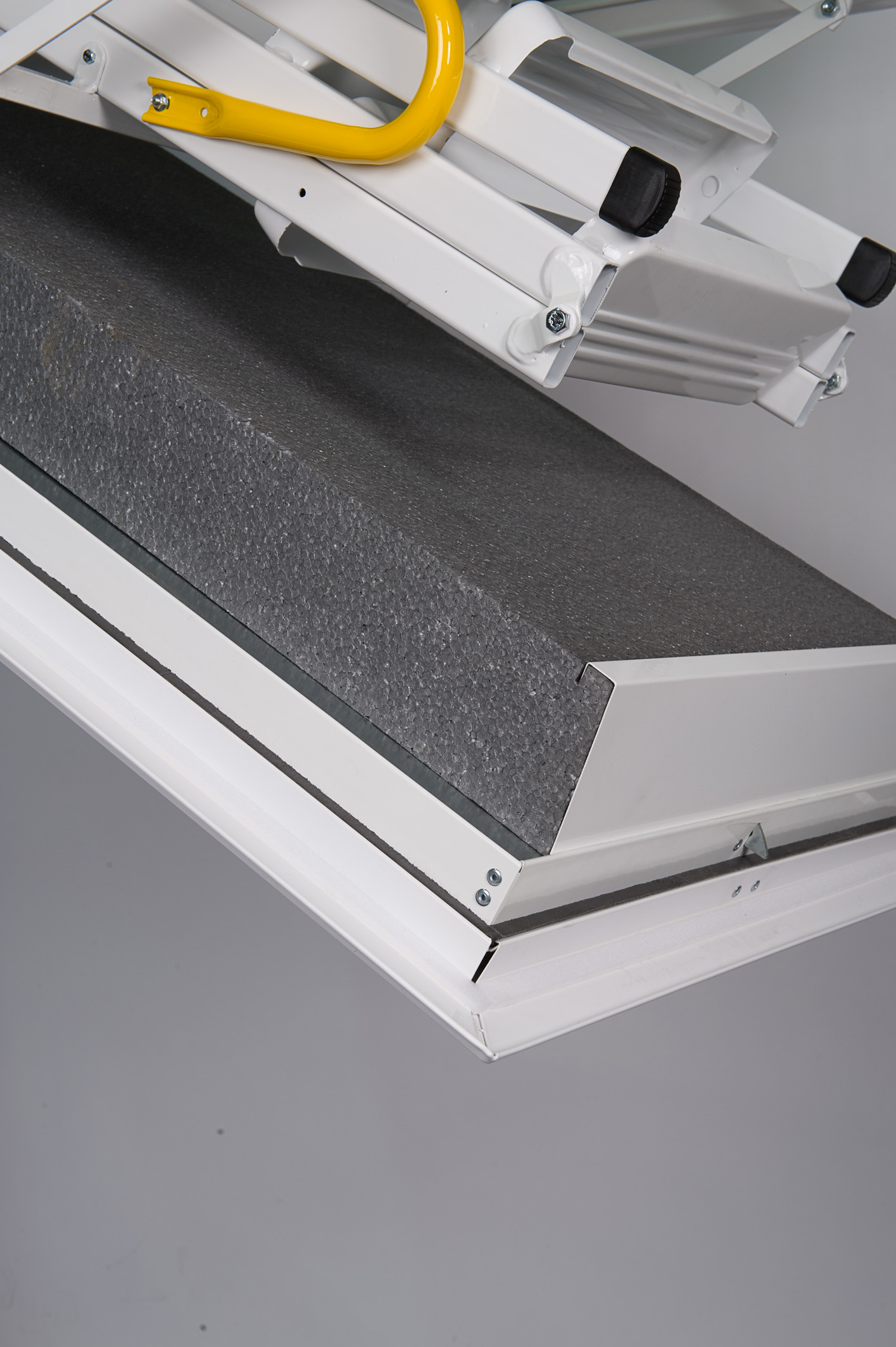 Close-up of the Arctic Fire attic ladder with heavily insulated grey trapdoor and white metal frame. The lower section of the folded steel ladder is visible.