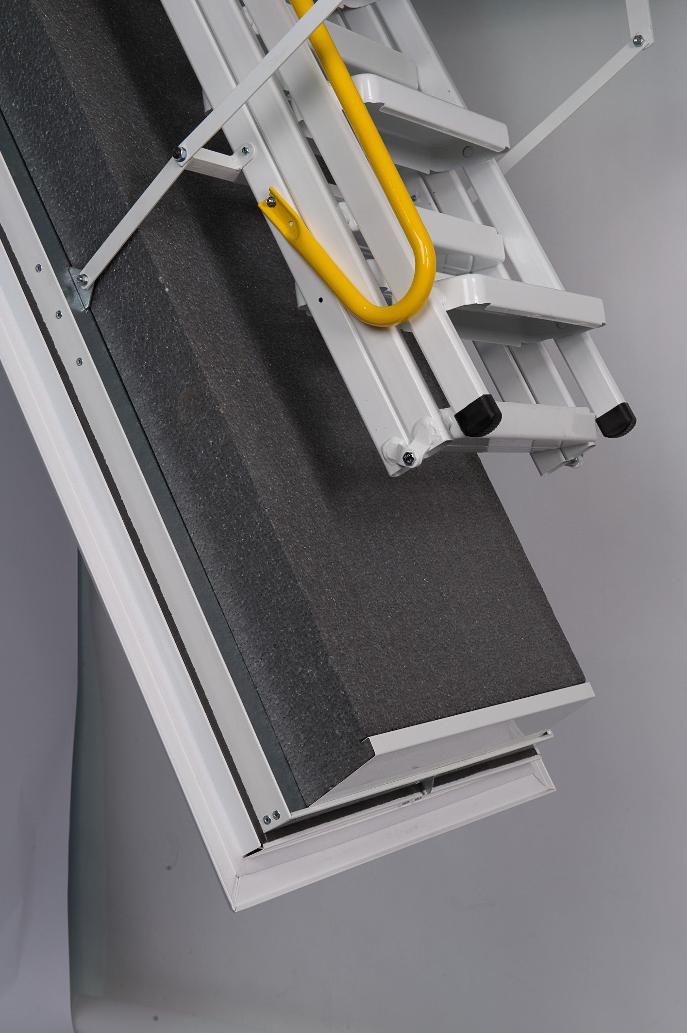 Detailed view of the Arctic Fire attic ladder with a dark grey insulated trapdoor, folded steel ladder, and yellow safety handle at the entry point.