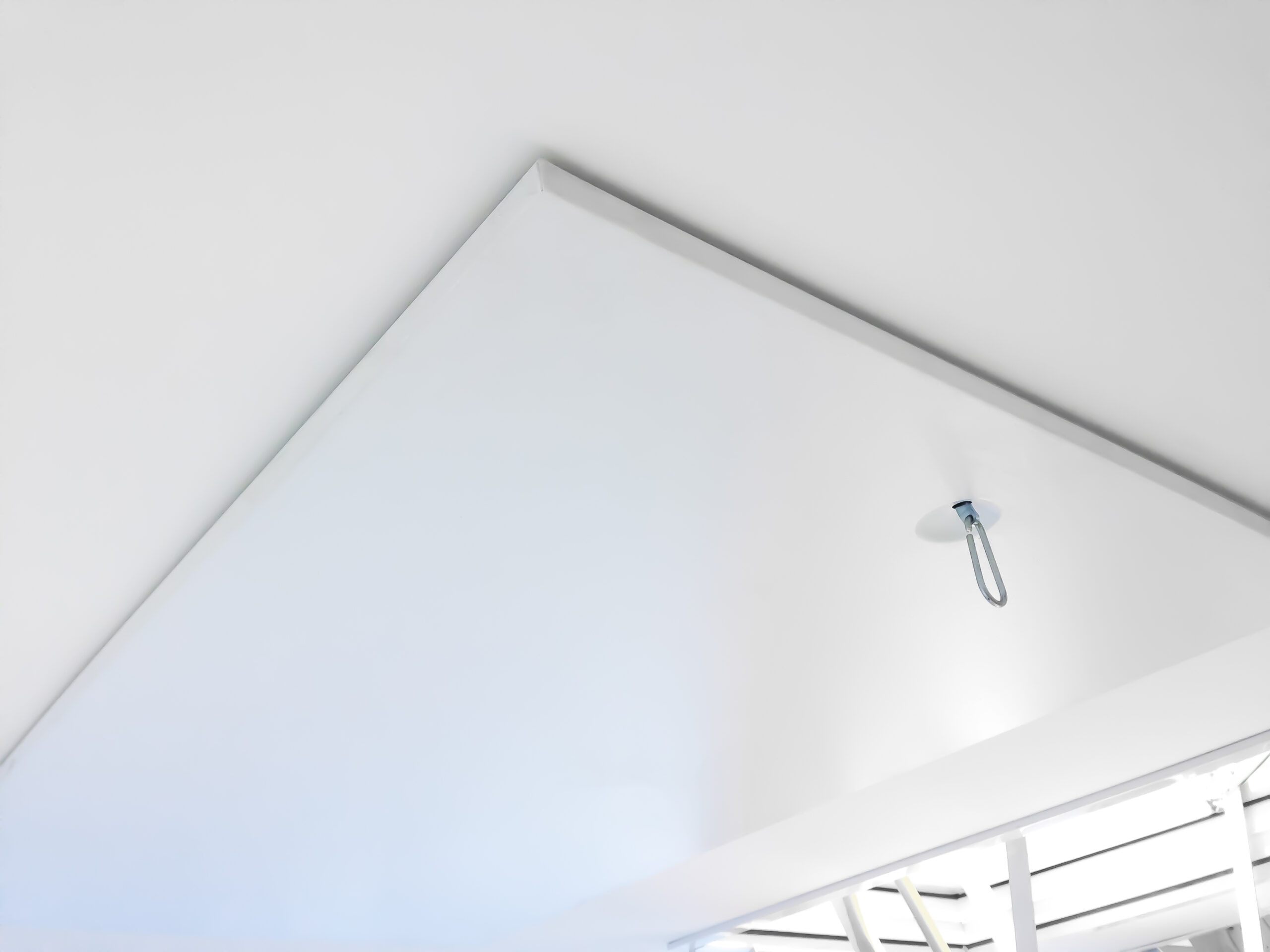 Detailed view of the closed Arctic Fire attic ladder from below. Visible is the flush-mounted white trapdoor with an integrated metal eyelet for opening the ladder.