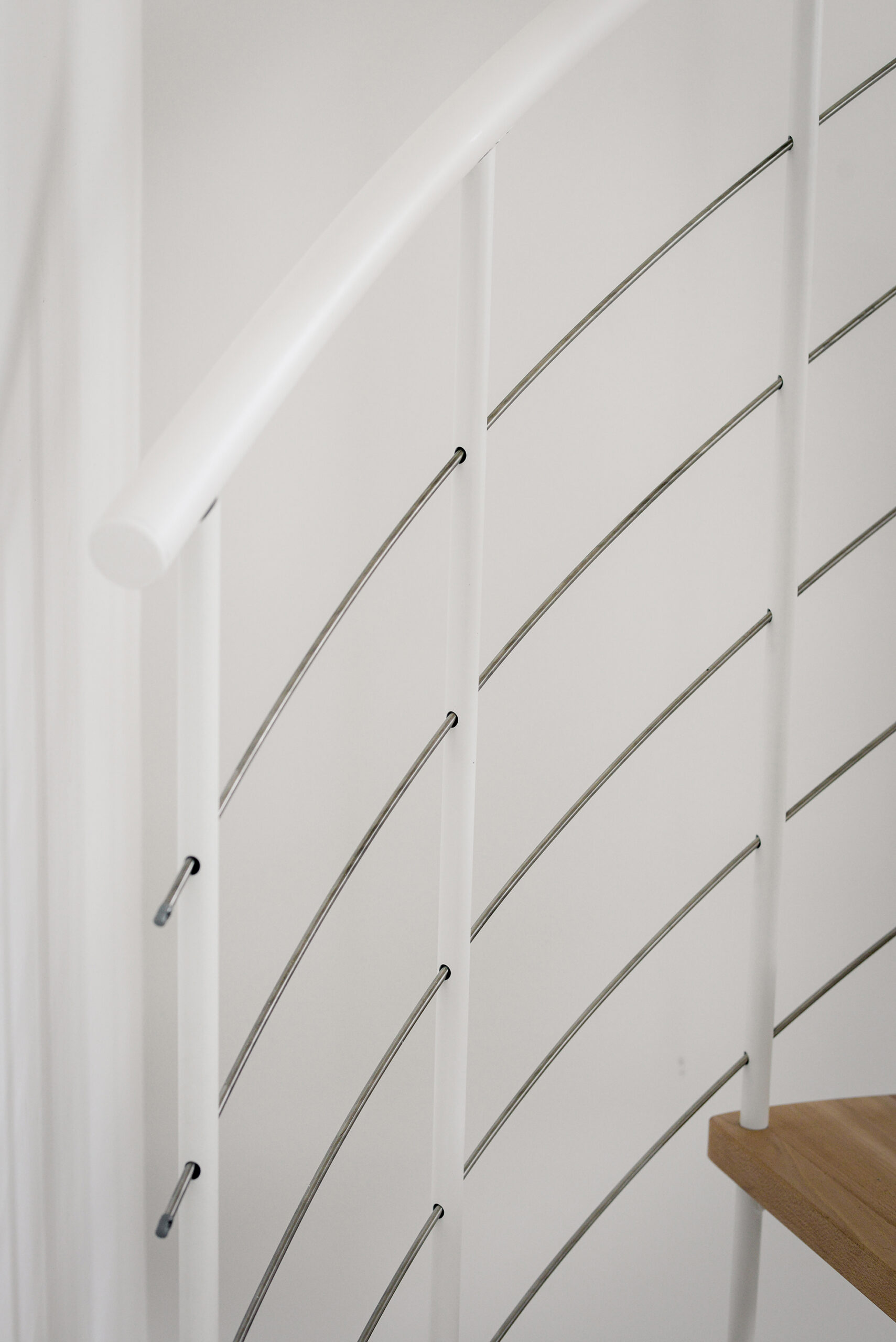 Close-up of the banister of the Venezia Smart spiral staircase. The vertical rods made of white powder-coated steel are crossed horizontally by 5 stainless steel bottom rails. The handrail is made of white PVC.