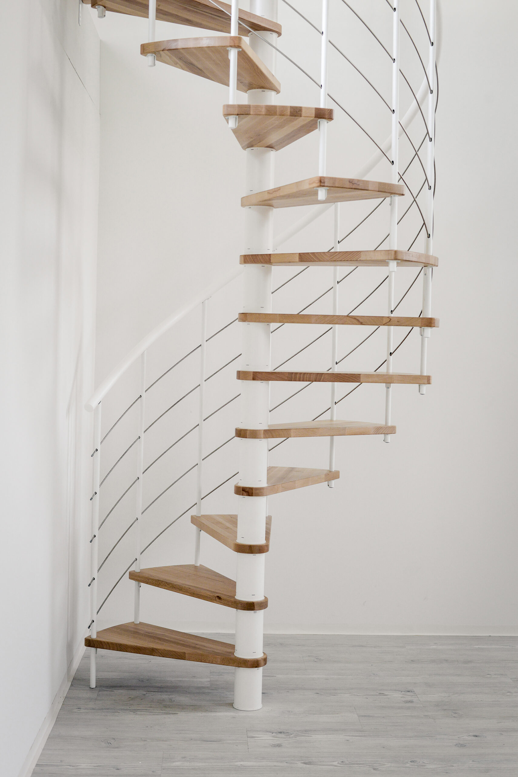 Venezia Smart spiral staircase in a white room viewed from the front. The steel banister in white looks discreet and the steps in beech wood stand out.