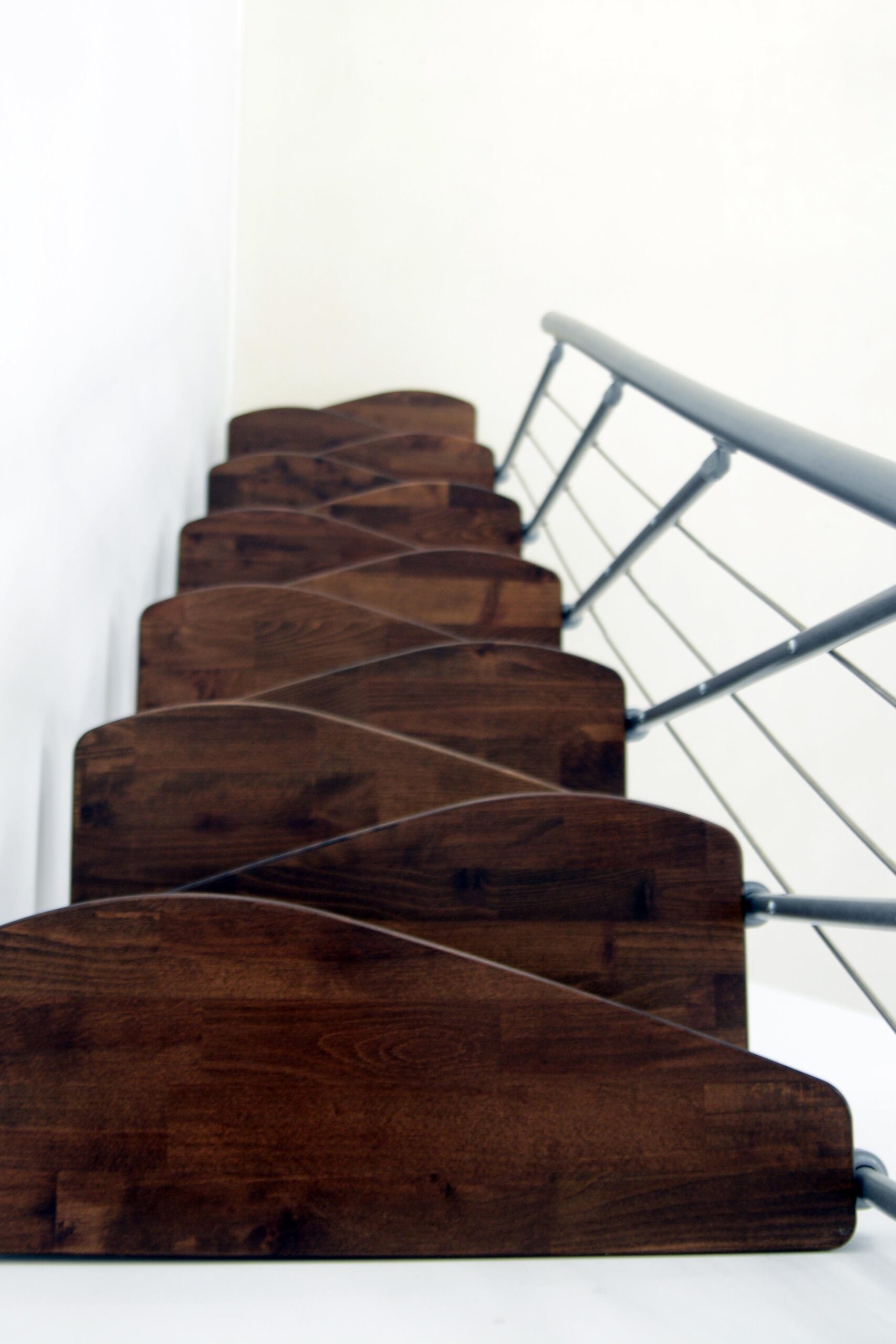 Top view of the Nizza space-saving staircase with alternating walnut-finish steps and a side metal railing with horizontal bars.
