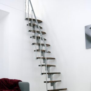 Straight Nizza space-saving staircase with alternating steps in walnut finish and a grey metal structure. The staircase is installed compactly along a white wall and features a side railing with horizontal bars and a grey handrail.