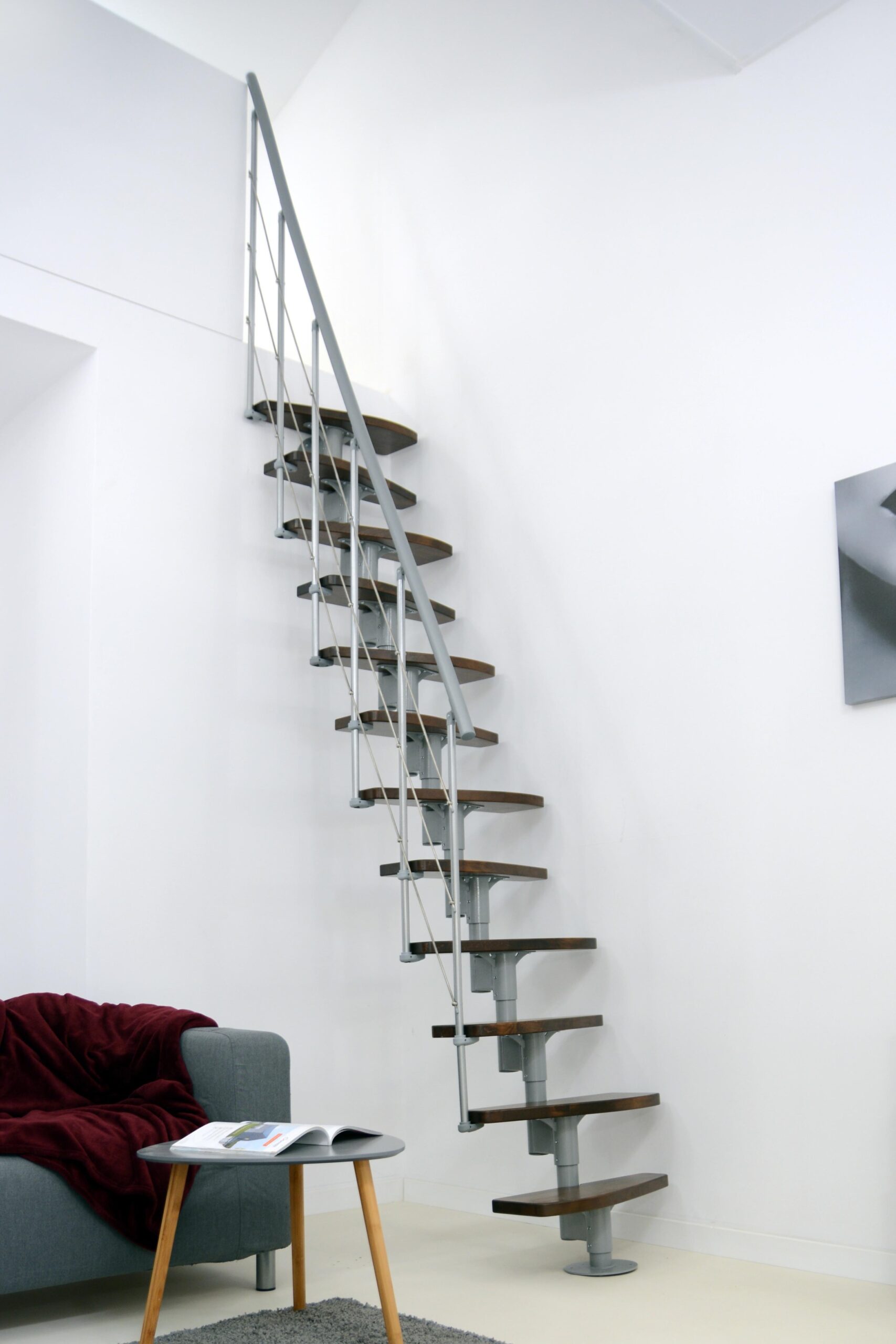 Straight Nizza space-saving staircase with alternating steps in walnut finish and a grey metal structure. The staircase is installed compactly along a white wall and features a side railing with horizontal bars and a grey handrail.