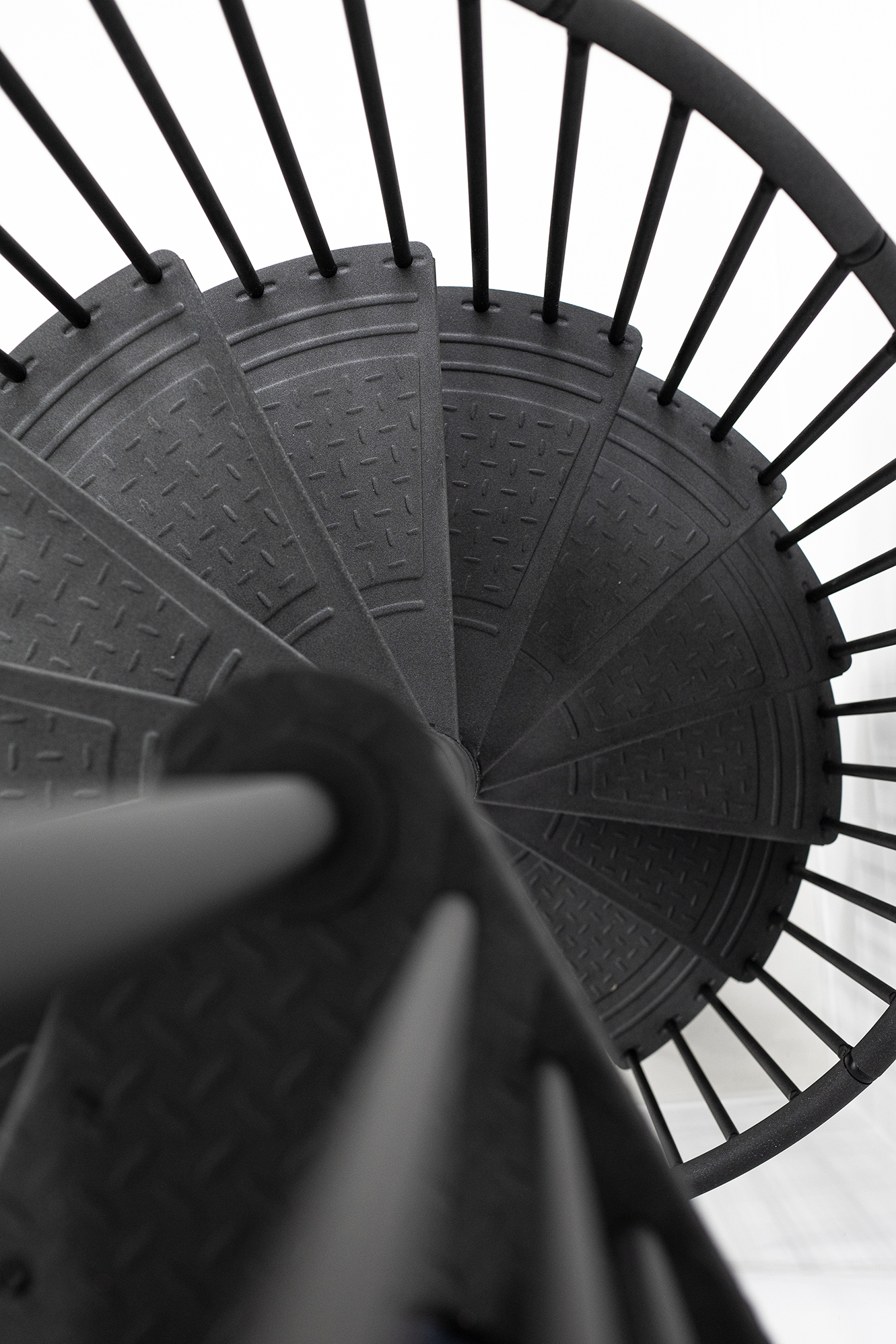 Detail view from above of the spiral staircase Rondo Color in anthracite. Visible are the anti-slip steps made of powder-coated metal with a tear plate structure and the vertical bar railing.