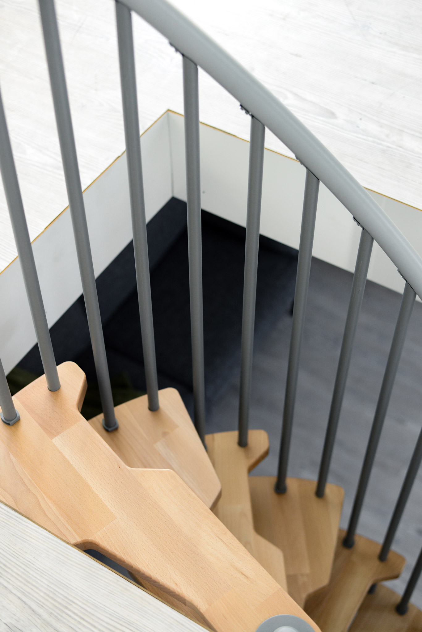 Top view of the exit area of the Metallica Smart spiral staircase. The grey railing bars and light wooden steps create a safe and modern design.