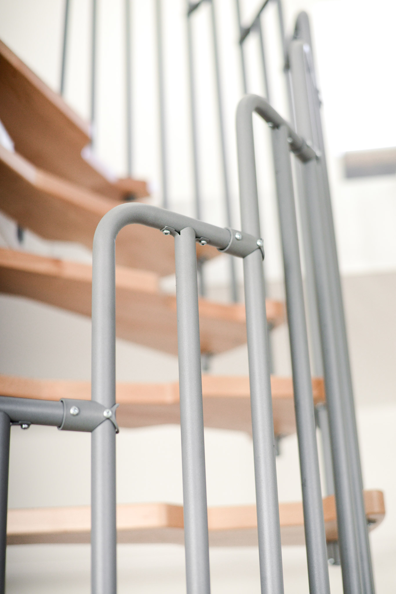Close-up of the grey railing of the Metallica spiral staircase. The sturdy metal construction ensures safety and complements the modern design with light wooden steps.