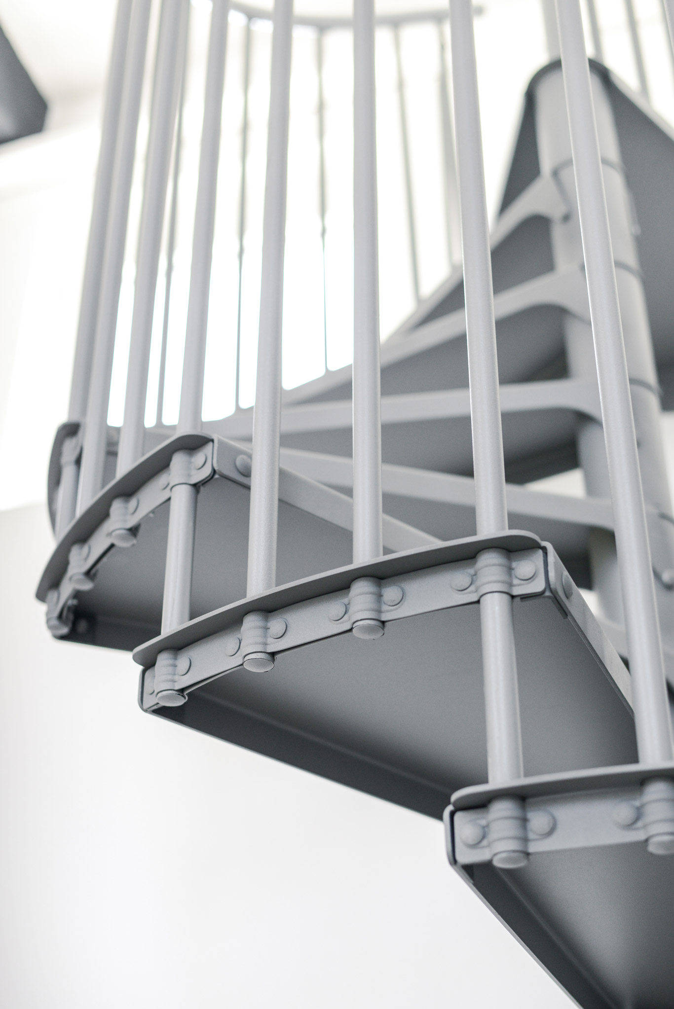 Detail view of the grey spiral staircase Rondo Smart. The focus is on the bolted metal steps and vertical railing rods. The solid construction highlights the high-quality finish of this space-saving metal spiral staircase.
