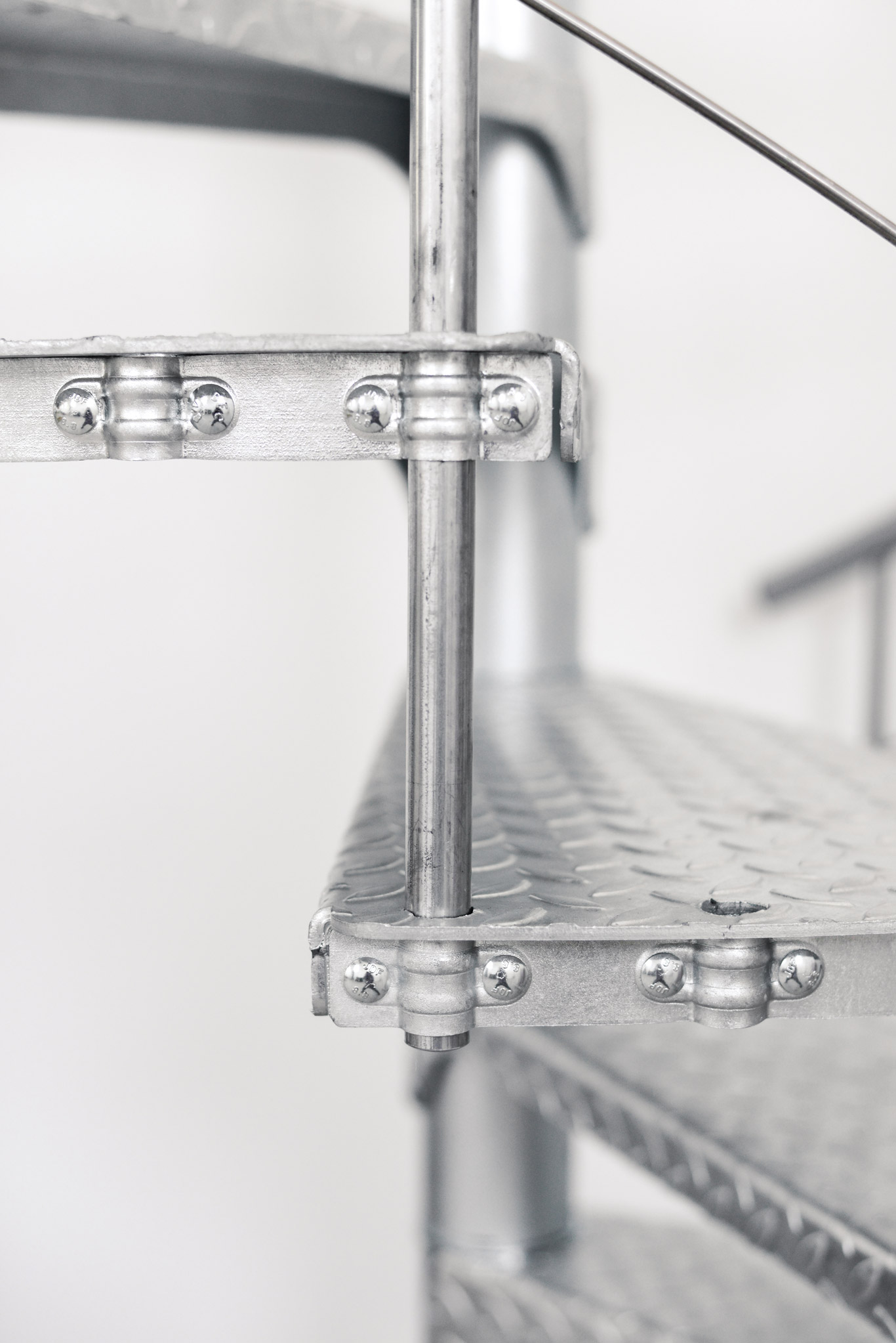 Close-up view of the Spino Zink Smart spiral staircase made of galvanized metal. The image shows a connection between the step and railing with clearly visible fastening elements.