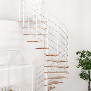 Fusion spiral staircase with beech steps and white metal banister built into a bright room with plants, cot and chair.
