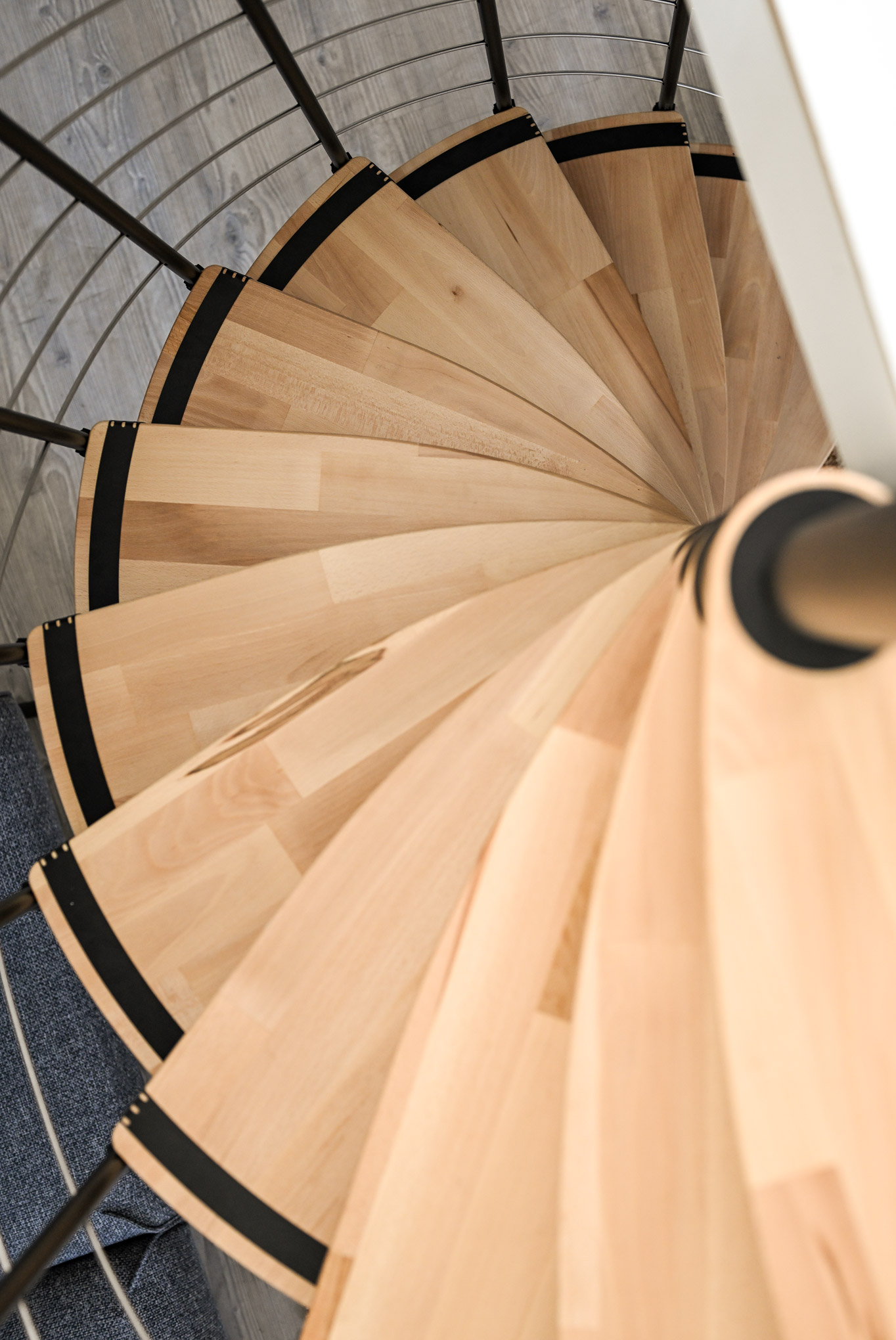 Top view of the Helios spiral staircase. The light wooden steps combined with black details create a harmonious, modern design. The round shape highlights the space-saving construction of the staircase.