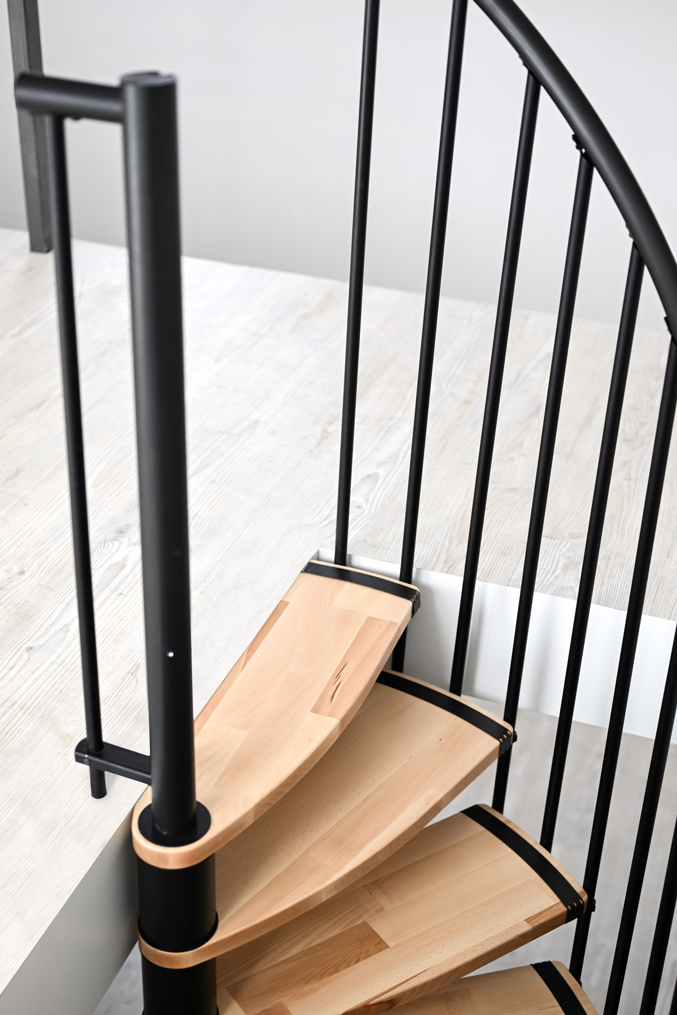 Close-up of the exit area of the Luna spiral staircase. The light wooden steps and black railing combine modern design with functionality, ensuring a safe transition to the upper floor.