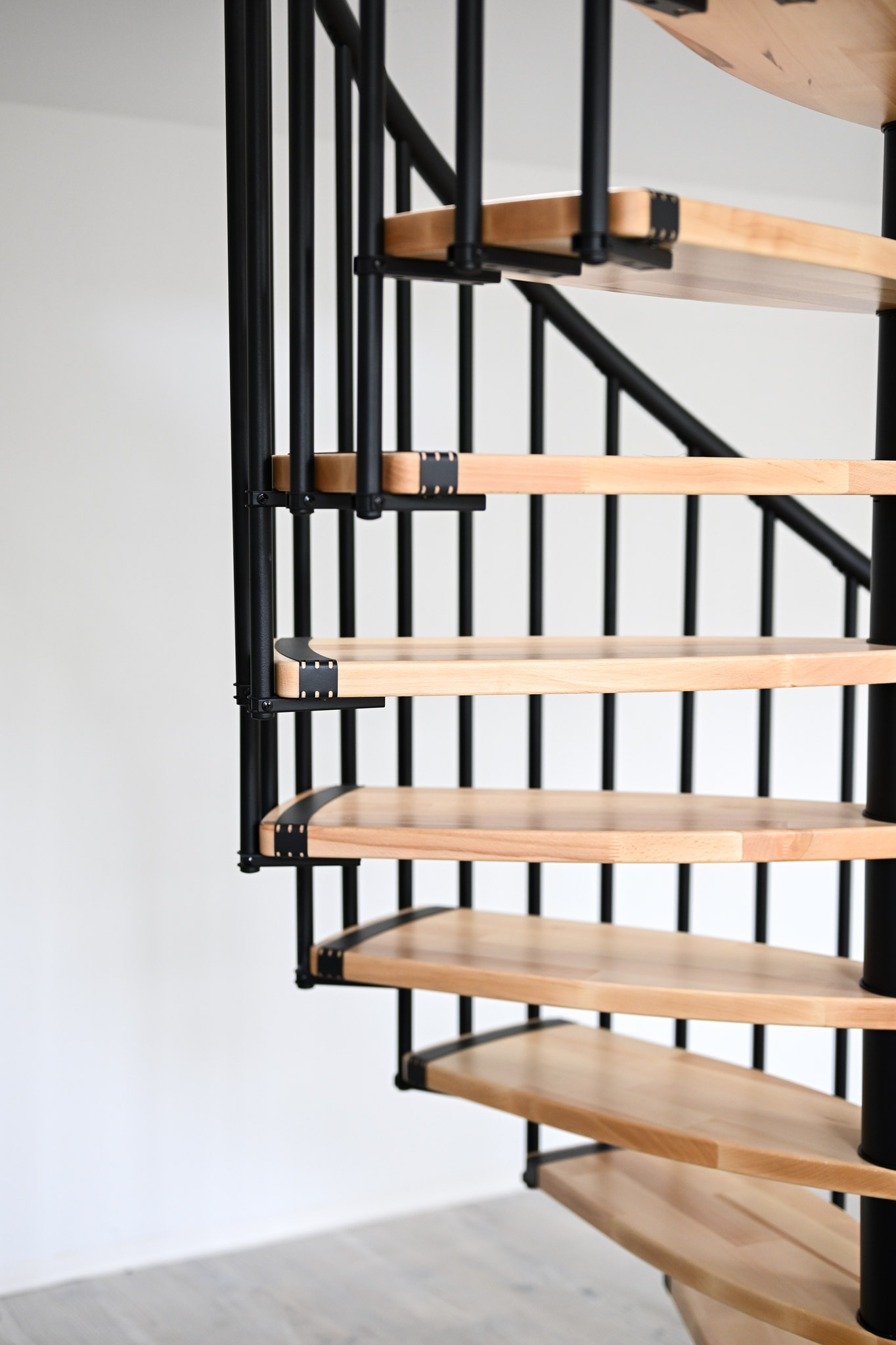 Side view detail of the Luna spiral staircase. The light wooden steps combined with black metal elements create a modern contrast and highlight the timeless design.