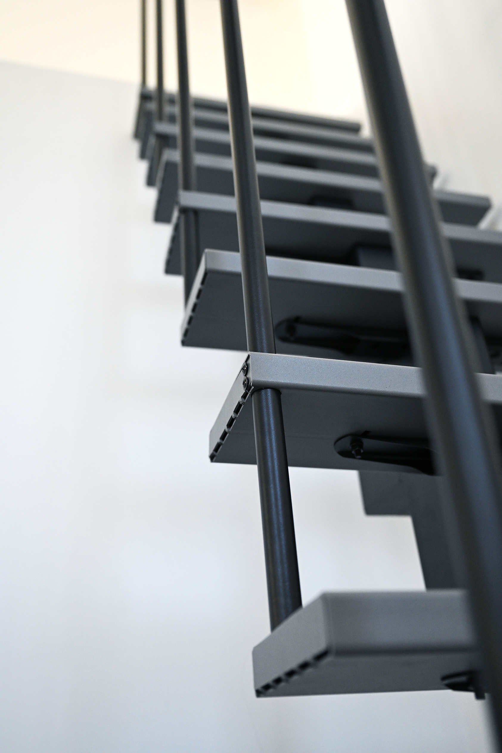 Close-up of a modern space-saving staircase with staggered grey metal steps and vertical black balusters, photographed from bottom to top.