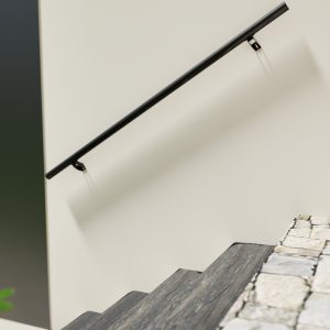 Side view of the Sirius handrail in anthracite, mounted on a light-colored wall along a modern staircase with dark steps and contrasting white stringers. The handrail is sleek, round, and supported by minimalist wall brackets.